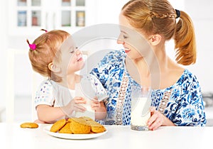 Happy family mother and baby daughter girl at breakfast: biscuits with milk