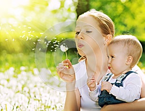 Happy family. Mother and baby girl blowing on a dandelion flower