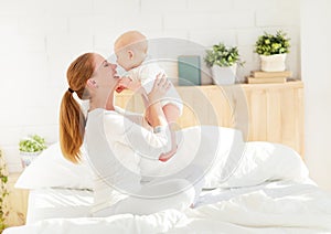 Happy family mother with baby playing and hug in bed