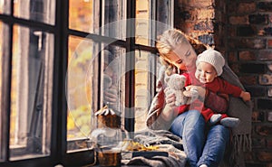 Happy family mother and baby playing and laughing at window in f