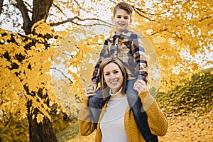 Happy family mother and child boy in the autumn leaf fall in park kid on the shoulder
