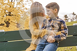 Happy family mother and child boy in the autumn leaf fall in park sit on bench