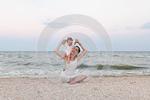 Happy family mother and child daughter doing yoga, meditate in lotus position on beach at sunset