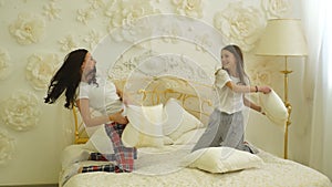 Happy family mother and child daughter playing on bed and pillow fight