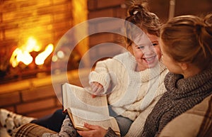 happy family mother and child daughter read book on winter evening near fireplace