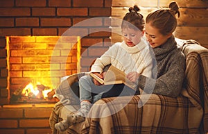 happy family mother and child daughter read book on winter evening near fireplace