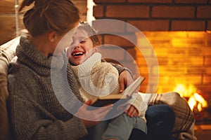 happy family mother and child daughter read book on winter evening near fireplace