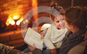 happy family mother and child daughter read book on winter evening near fireplace.