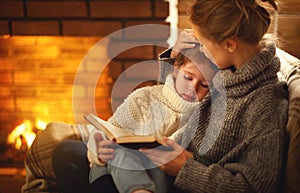 happy family mother and child daughter read book on winter evening near fireplace