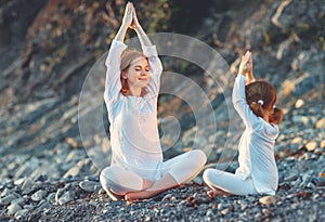 Happy family mother and child doing yoga, meditate in lotus position on beach