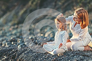 Happy family mother and child doing yoga, meditate in lotus position on beach