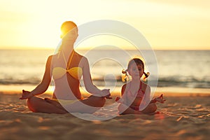 Happy family mother and child doing yoga, meditate in lotus position on beach .