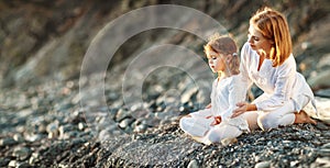 Happy family mother and child doing yoga, meditate in lotus position on beach