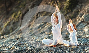 Happy family mother and child doing yoga, meditate in lotus position on beach