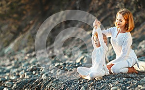 Happy family mother and child doing yoga, meditate in lotus position on beach