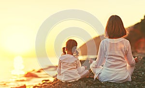 Happy family mother and child doing yoga, meditate in lotus position on beach