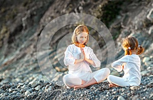 Happy family mother and child doing yoga, meditate in lotus position on beach