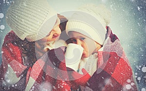 happy family mother and child drinking hot tea on winter walk outdoors