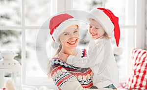 Happy family mother and child girl hugs at window at the winter