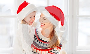 Happy family mother and child girl hugs at window at the winter