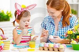 Happy family mother and child girl paints eggs for Easter