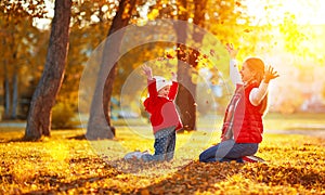 Happy family mother and child girl playing and throw leaves in a
