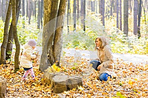 Happy family mother and child girl playing throw leaves in autumn park outdoors