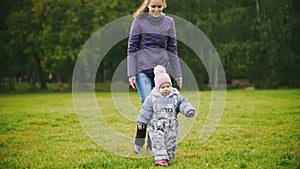 Happy family: Mother and child - little girl walking in autumn park: baby playing at the grass, slow motion