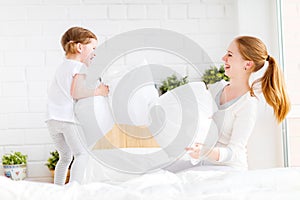 Happy family mother and child playing on bed and pillow fight