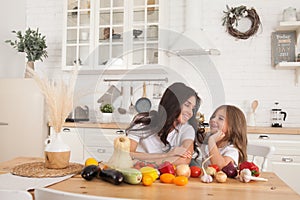 Happy family mother and child posing at home. Beautiful young mom and little daughter having fun and preparing vegetables for