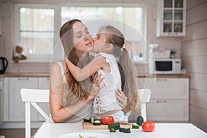 Happy family mother and child posing at home. Beautiful young mom and little daughter having fun and preparing vegetables for