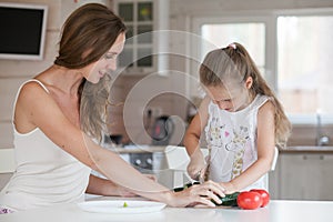 Happy family mother and child posing at home. Beautiful young mom and little daughter having fun and preparing vegetables for