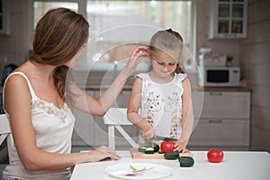 Happy family mother and child posing at home. Beautiful young mom and little daughter having fun and preparing vegetables for