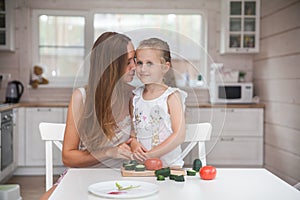 Happy family mother and child posing at home. Beautiful young mom and little daughter having fun and preparing vegetables for