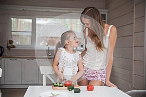 Happy family mother and child posing at home. Beautiful young mom and little daughter having fun and preparing vegetables for
