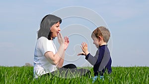 Happy family: mother and child sit on green grass and play, slapping each other on Batty