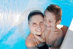 Happy family of mother and child smiling and embrace in blue swimming pool in summer vacation