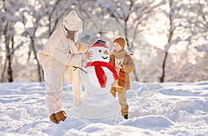 happy family mother and child son make a snowman and have fun on a winter walk in the park
