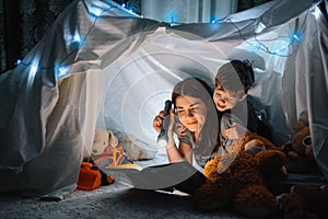 Happy family mother and child son reading a book with a flashlight in a tent at home. family concept