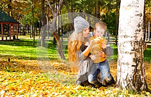 Happy family: mother and child sonr have fun in autumn on autumn park. Young Mother and kid girl hugging in leaves at fall.