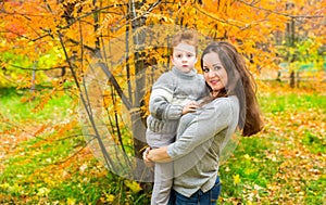 Happy family: mother and child sonr have fun in autumn on autumn park. Young Mother and kid girl hugging in leaves at fall.