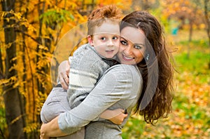 Happy family: mother and child sonr have fun in autumn on autumn park. Young Mother and kid girl hugging in leaves at fall.