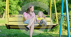 Happy family, mother and child swinging on a swing in the city park