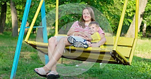 Happy family, mother and child swinging on a swing in the city park