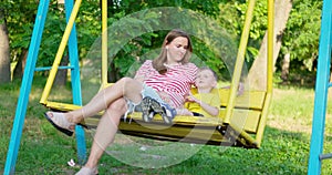 Happy family, mother and child swinging on a swing in the city park