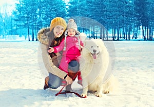 Happy family mother and child with white Samoyed dog walking in winter