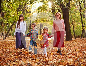 Happy family, mother with children, daughters and son walking through fallen leaves of autumn city forest park
