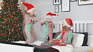 happy family mother and children in pajamas opening gifts on christmas morning near tree