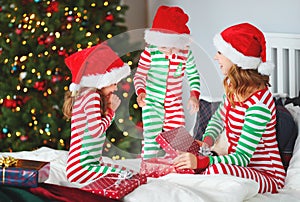 Happy family mother and children in pajamas opening gifts on christmas morning near christmas tree