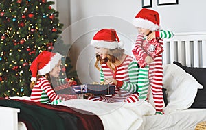 happy family mother and children in pajamas opening gifts on christmas morning near tree
